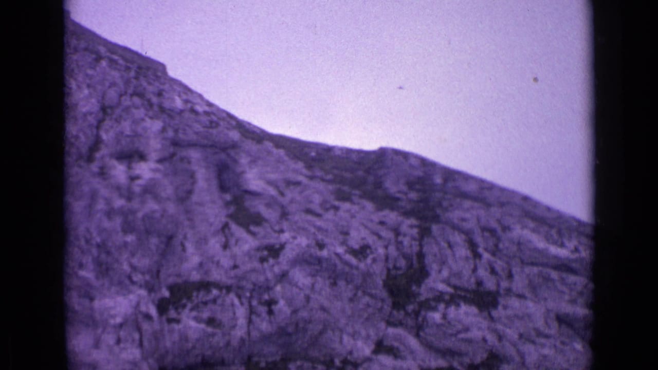 Swiss 8mm home-movie frame showing a steep rocky mountainside, pale sky, and visible mid-century film texture.