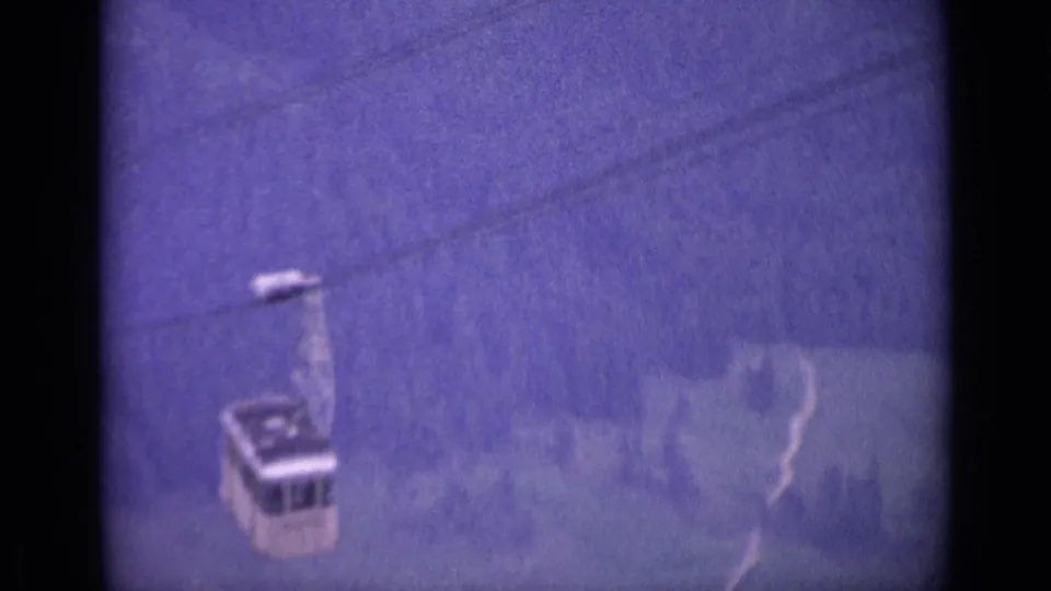 1962 Switzerland 8mm frame showing a small white cable car moving down over wooded alpine terrain with a purple film cast.