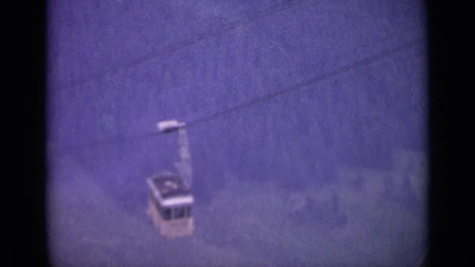 The descending cable car sits lower in the frame, with soft-focus woods and heavy grain characteristic of 1962 8mm travel footage.