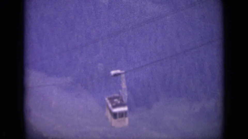 Final frame of the 1962 Swiss cable car descent, with the cabin near the lower edge and wooded alpine terrain filling the background.