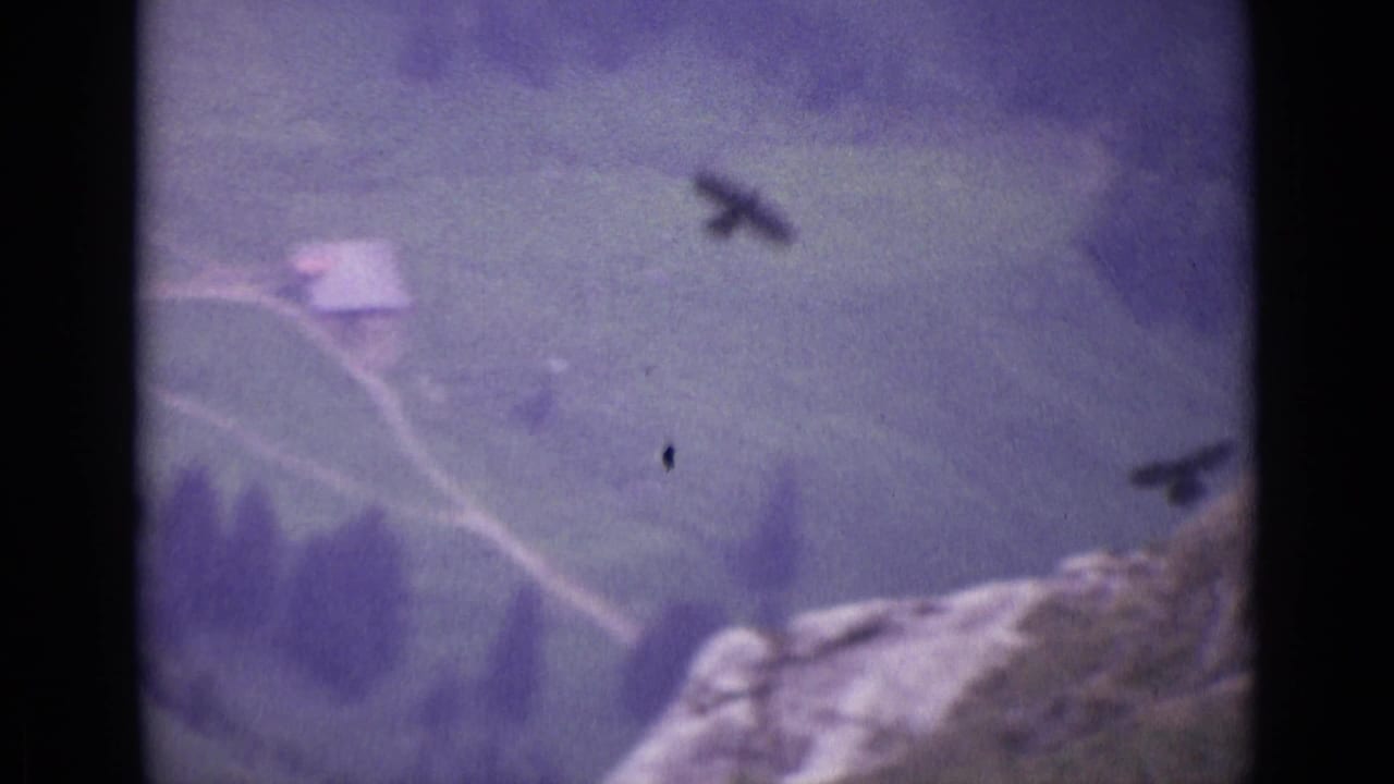 1962 Swiss Alps 8mm frame showing a distant dark bird above a misty mountain valley and rocky foreground.