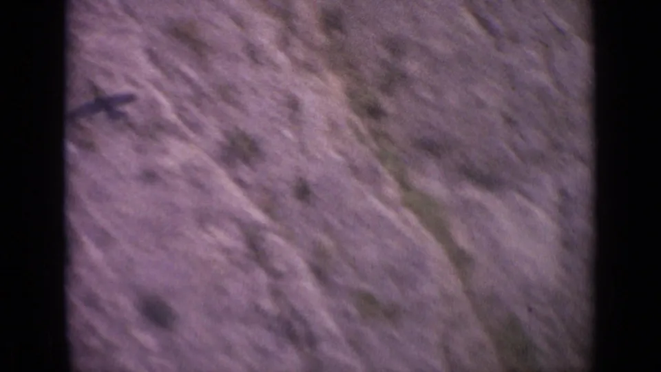 1962 Switzerland 8mm frame with a dark bird shape or shadow near the edge of rugged valley terrain.