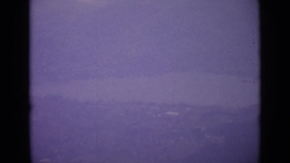 A soft, hazy view of distant mountains and valley terrain appears in purple-shifted 1962 Switzerland 8mm footage.