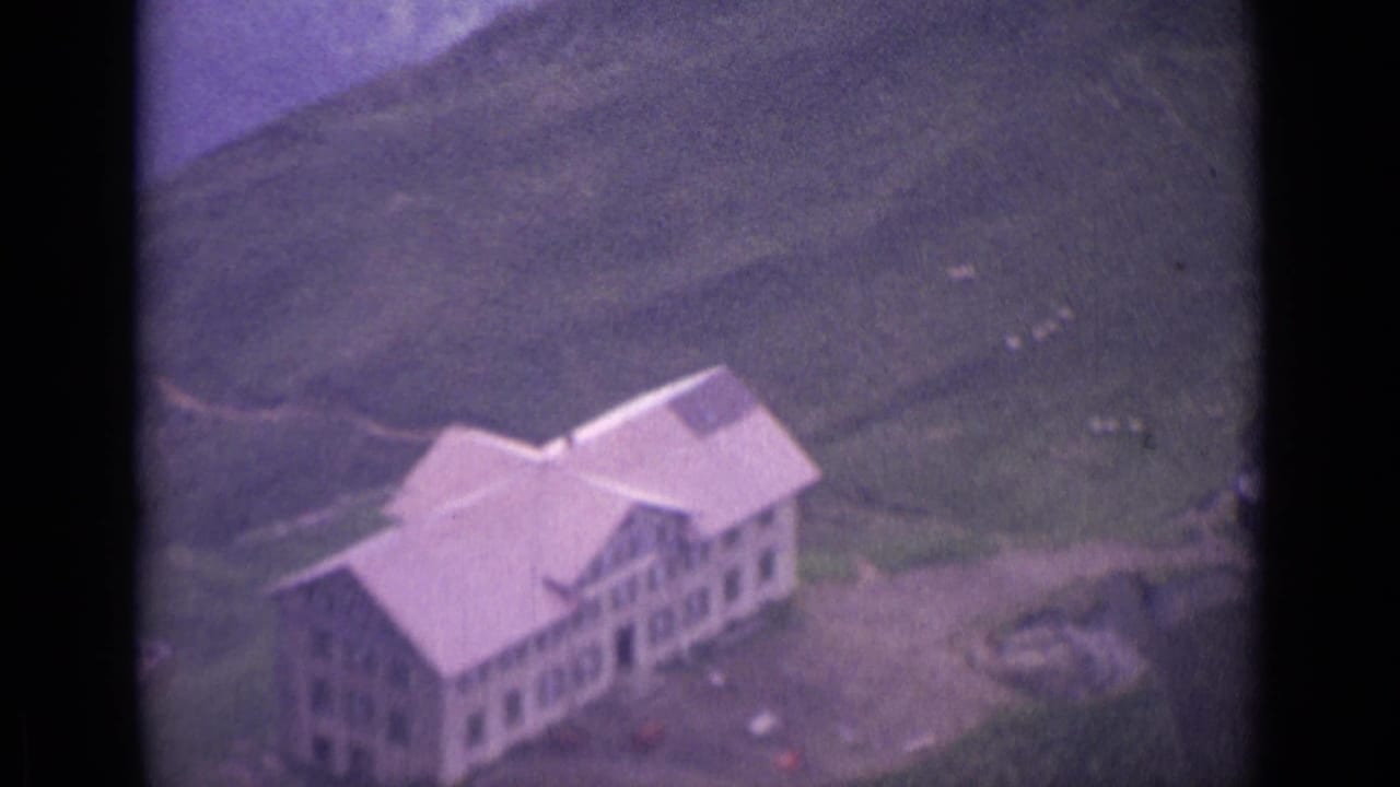 Aerial view of a large alpine building on a grassy hillside.