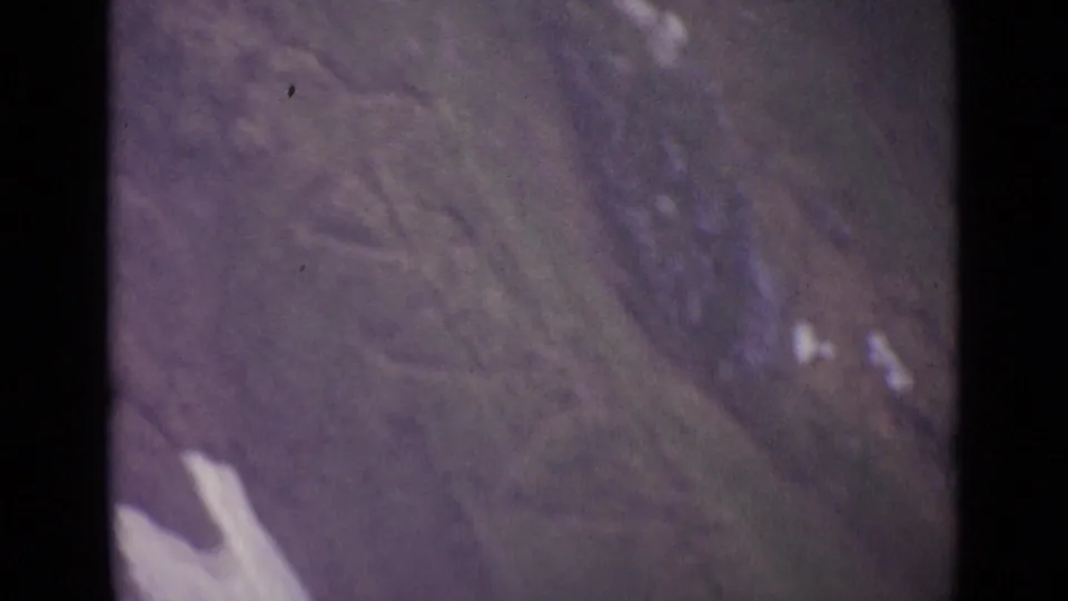 1962 Swiss aerial home-movie frame showing open alpine hillside and a pale snow or rock patch near the lower edge.