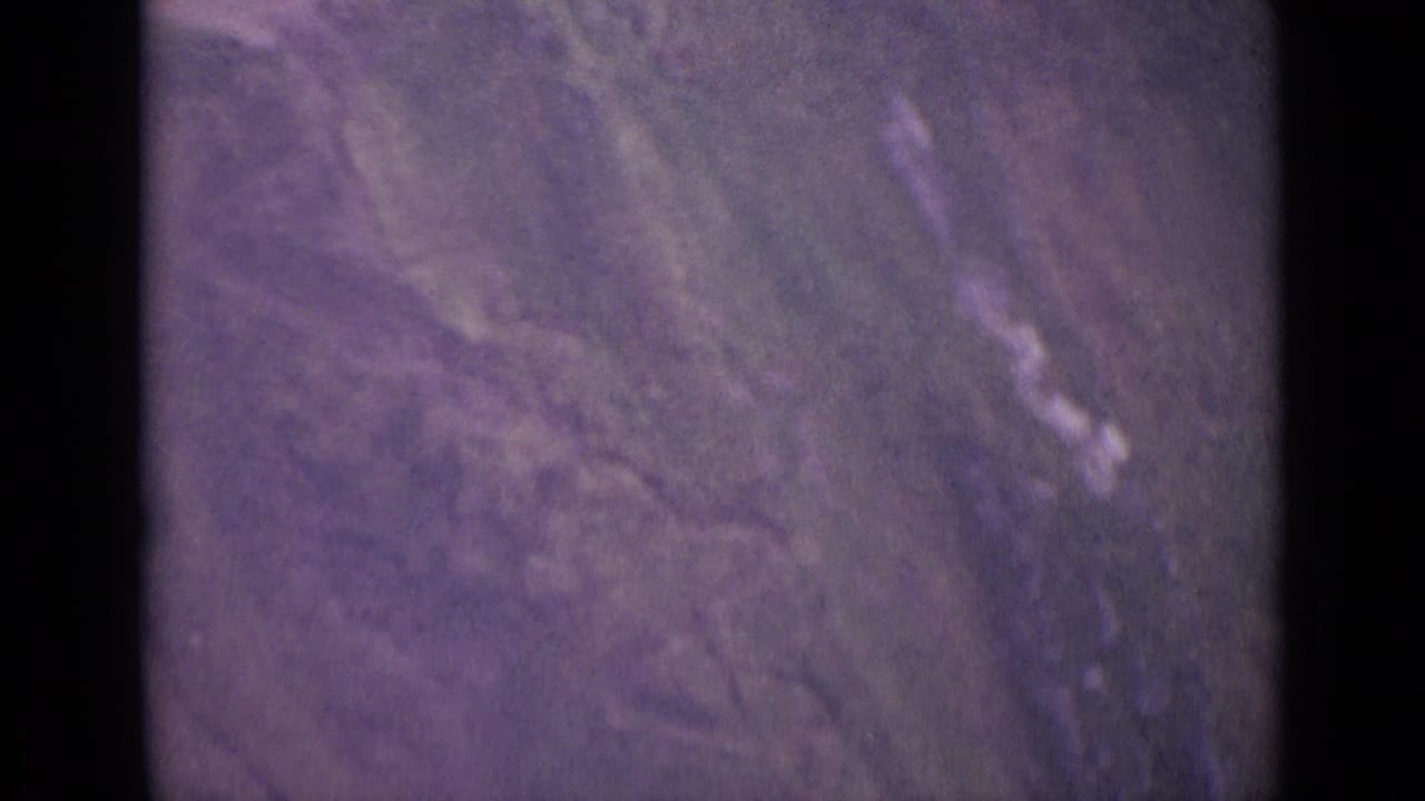Soft, purple-tinted view of a steep grassy mountain slope with dark film-frame edges.