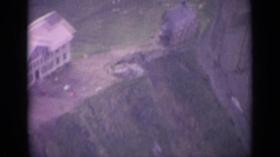 1962 Swiss home-movie frame with rustic buildings, paths and trees on a remote mountain slope.
