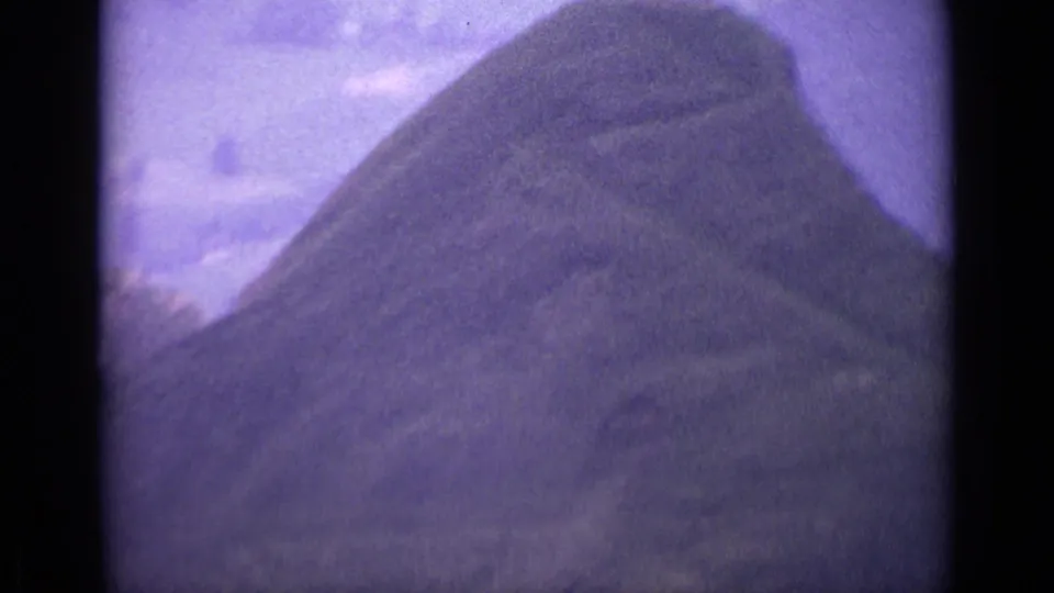 Purple-shifted 1962 Swiss 8mm frame looking over a rounded grassy rise in a mountain landscape.
