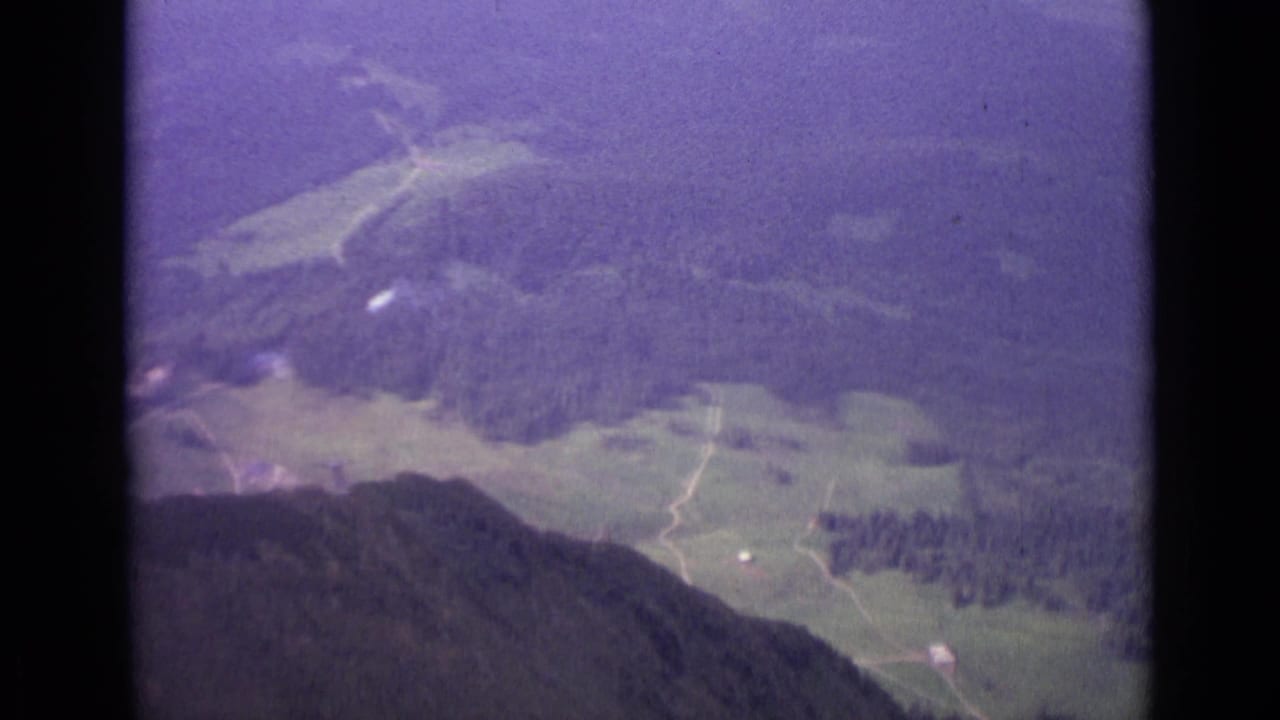High valley view with forests, pale roads, meadows, and dark mountain slope in foreground.