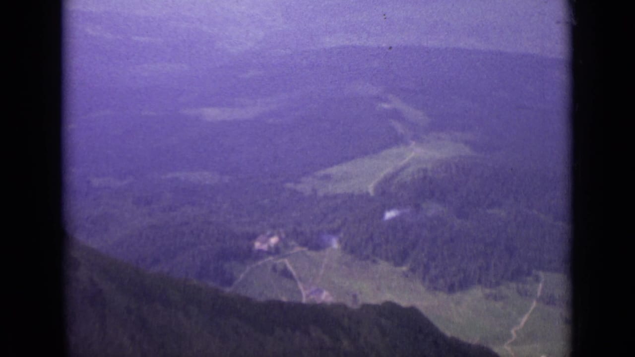 1962 Switzerland 8mm frame showing a distant alpine valley, slopes, and hazy mountains with strong purple film shift.