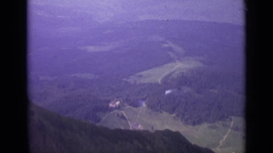 1962 Switzerland 8mm frame showing a distant alpine valley, slopes, and hazy mountains with strong purple film shift.