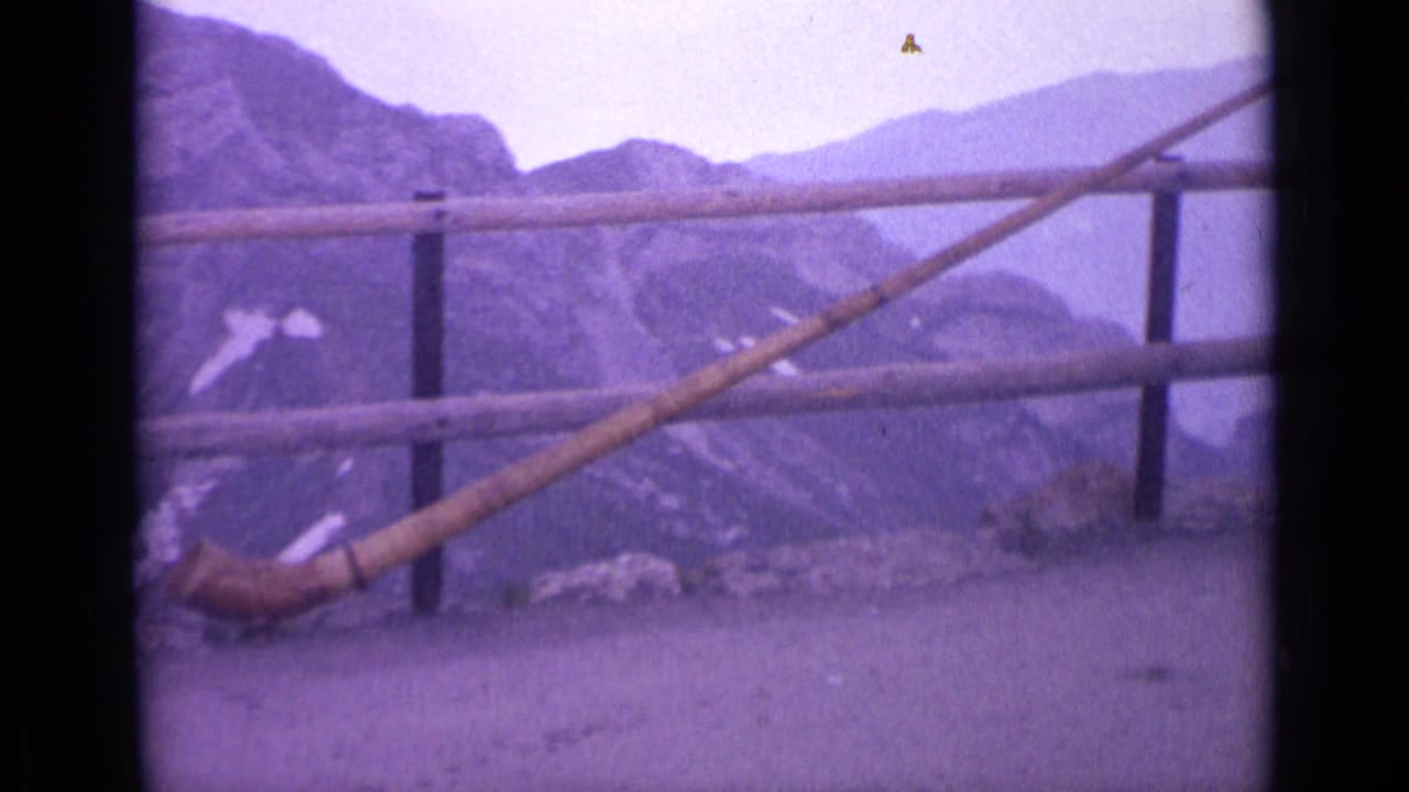 1962 Switzerland home-movie frame showing the horn set near the ground at an overlook, framed by railing and distant alpine slopes.