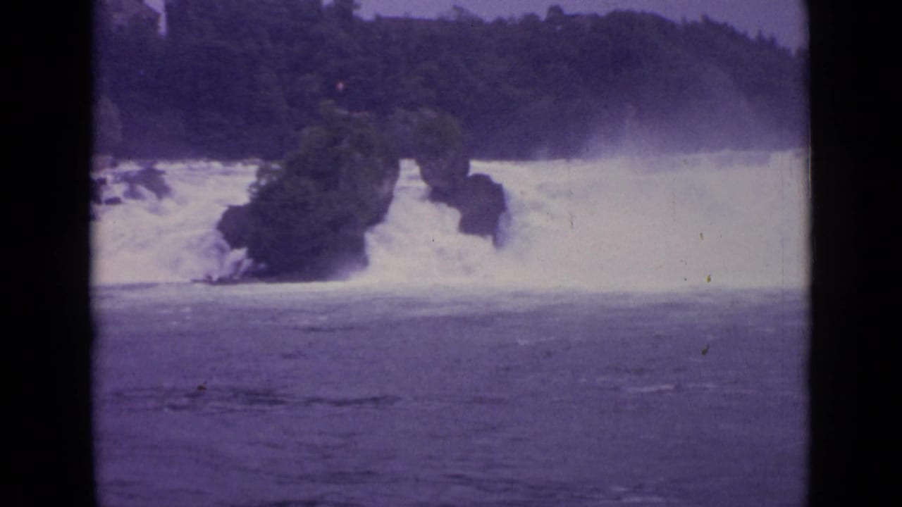 Broad river water faces a foaming spillway and wooded shoreline.