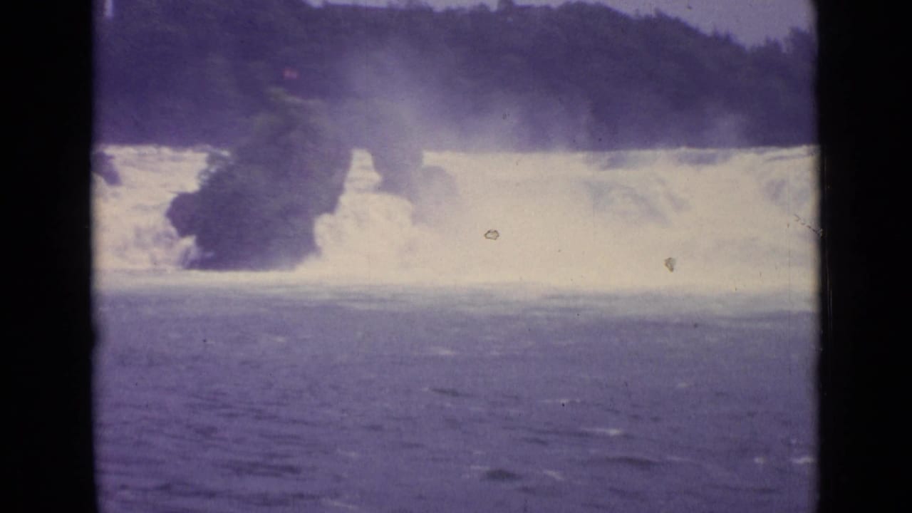 8mm footage from Switzerland in 1962 showing overexposed white rapids, mist, and a dark wooded rock mass in the current.