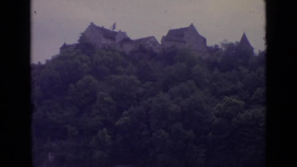 1962 Switzerland 8mm frame with stone castle buildings silhouetted along the top of a tree-covered hill.