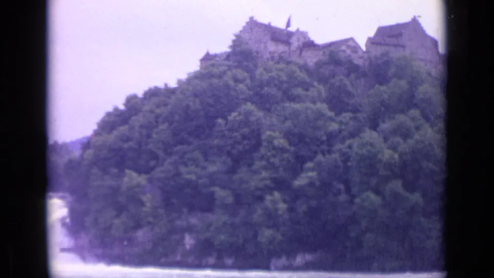 1962 Switzerland 8mm frame showing a hilltop castle above dense woods with a glimpse of river below.