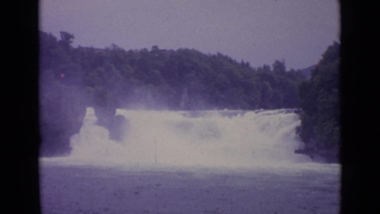 Waterfall cascading through a wooded gorge with mist and dark film borders.