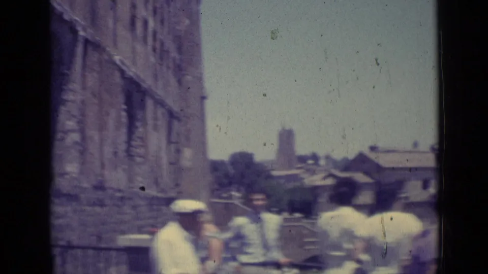 1962 Vatican City visitor footage showing tourists in light clothing beside a stone wall, with distant architecture and soft 8mm fading.