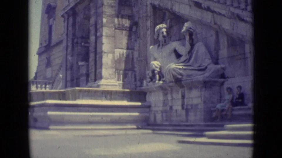 1962 Vatican City footage showing a seated stone sculpture, broad steps, church stonework, and visitors seated near the edge of the frame.