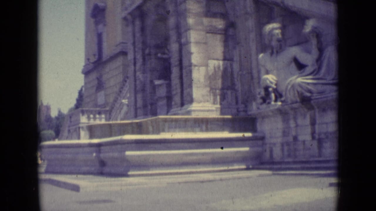 Seated classical statue beside a large stone building and sunlit steps.
