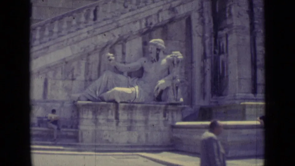 1962 Vatican City frame showing the seated classical statue near monumental steps, with an incidental pedestrian passing at the edge.