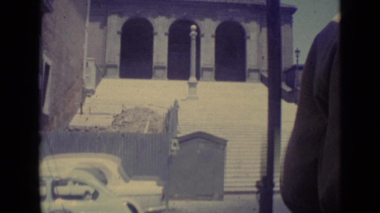 Wide stone steps leading to arched entrances, with a light-colored car and street lamps in front.