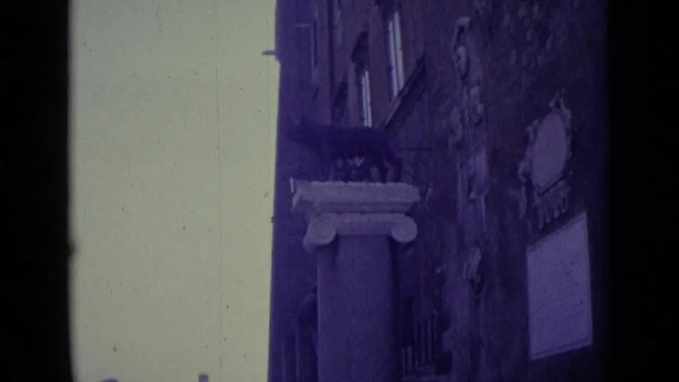1962 Vatican City home-movie frame showing a narrow architectural passage with a column base, wall-mounted signs, and heavy frame borders.