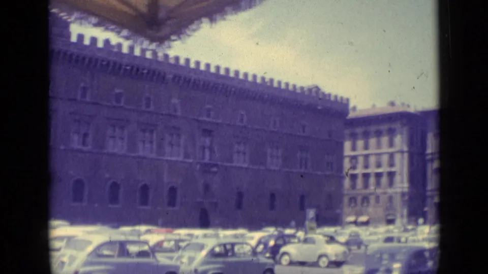 1962 Vatican City home-movie view of a palace facade and busy parking area with compact European cars.