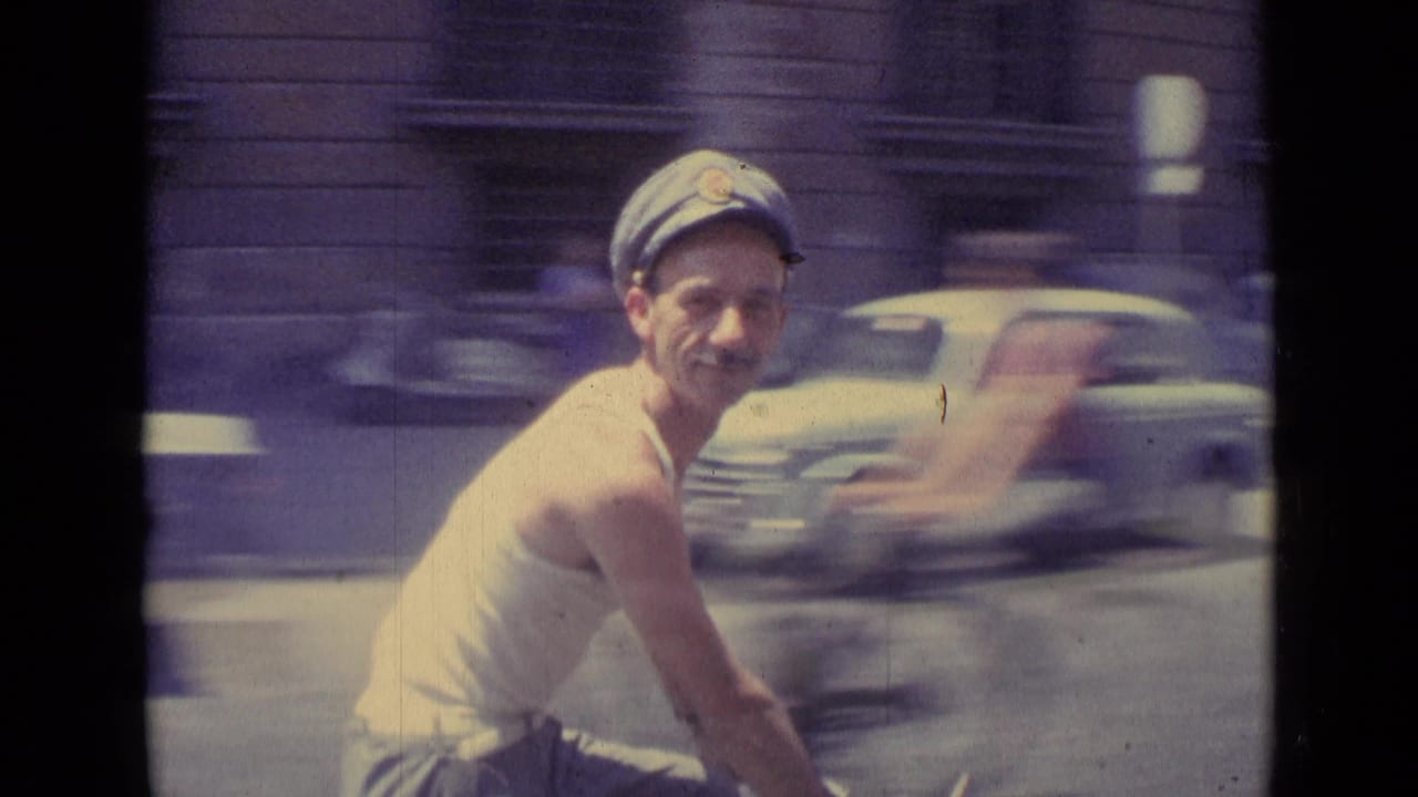 Close 1962 Vatican City home-movie view of a smiling cart rider in a cap, with passing cars blurred in the background.