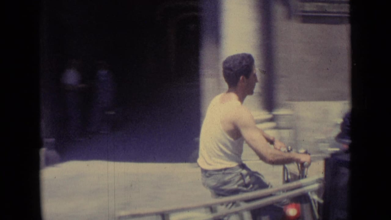 Scooter rider passes a shaded entrance and building wall on a bright street.