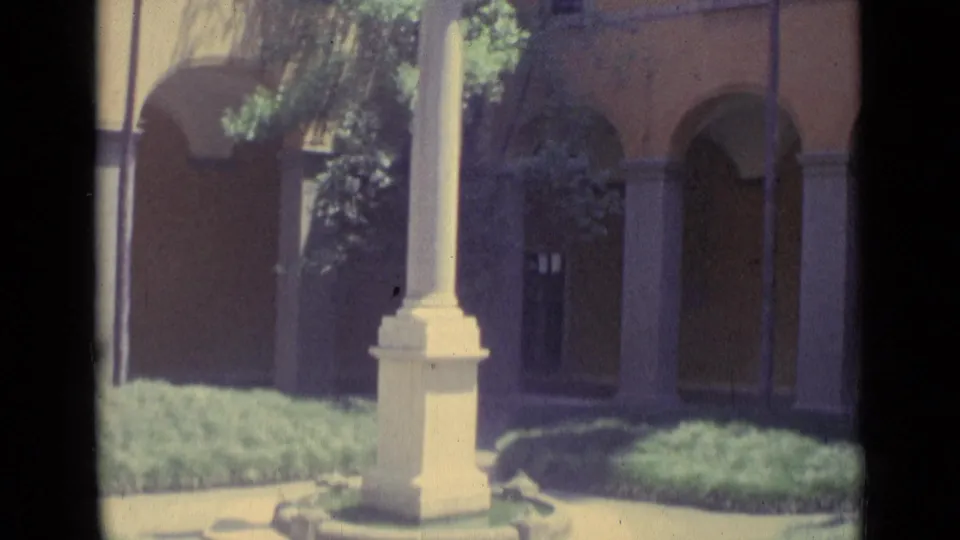 1962 Vatican City frame with arched colonnades, a white column base, garden shrubs, and palm shadows across warm walls.