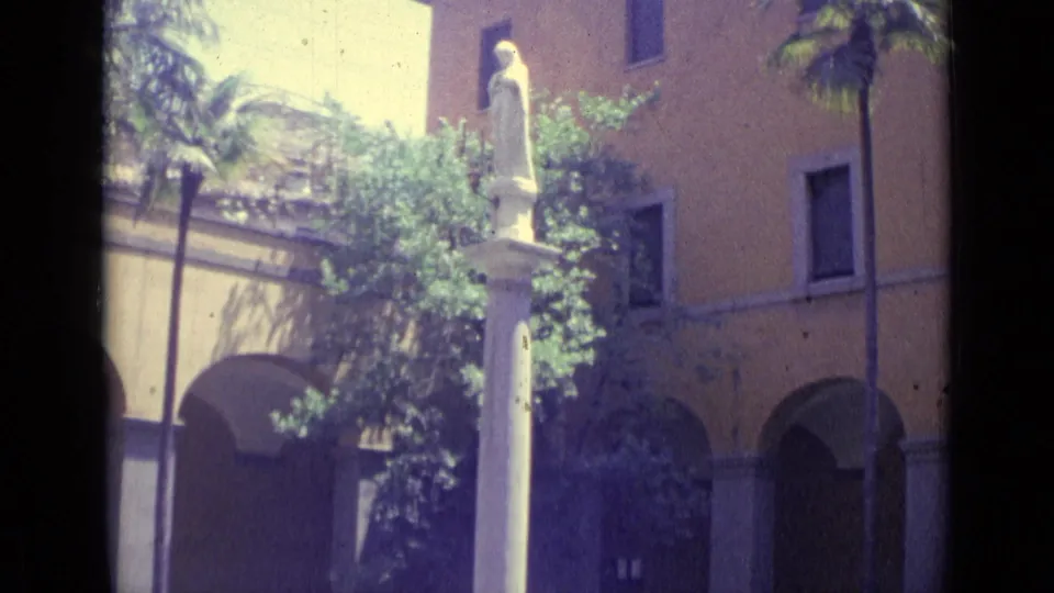 1962 Vatican City frame showing a robed statue on a white column above an arched courtyard with trees, palms, and warm-toned walls.