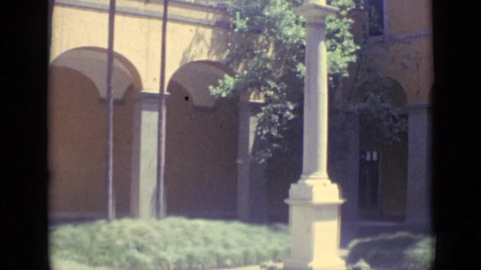 Vatican City courtyard detail with arched colonnades, a statue column, doorway, greenery, and strong midday light.
