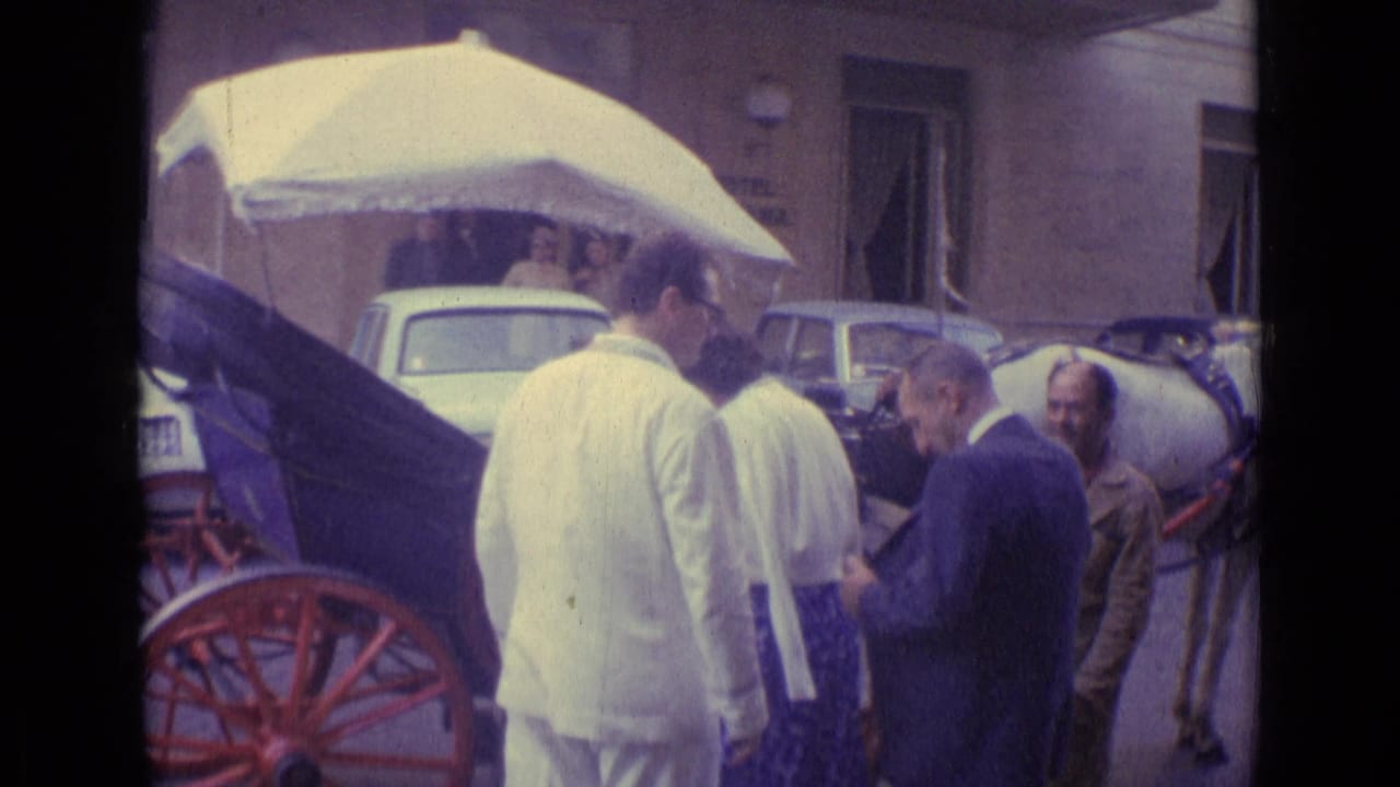 Vatican City home-movie frame of visitors clustered around a white-canopy carriage, with a horse partly visible and cars behind.