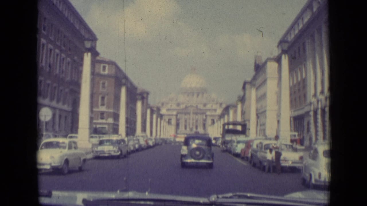 A broad street lined with parked cars leads toward a domed basilica.