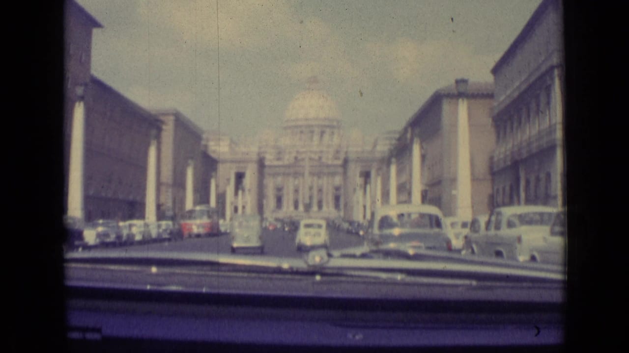 View through a car windshield toward St. Peter's Basilica with traffic and parked cars ahead.