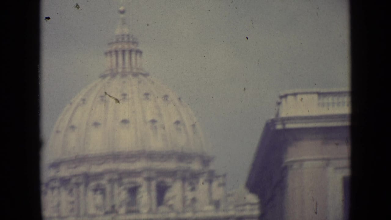 1962 Vatican City home-movie frame showing the dome of St. Peter's Basilica in soft focus behind dark window-like edges.