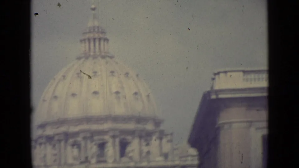 1962 Vatican City home-movie frame showing the dome of St. Peter's Basilica in soft focus behind dark window-like edges.