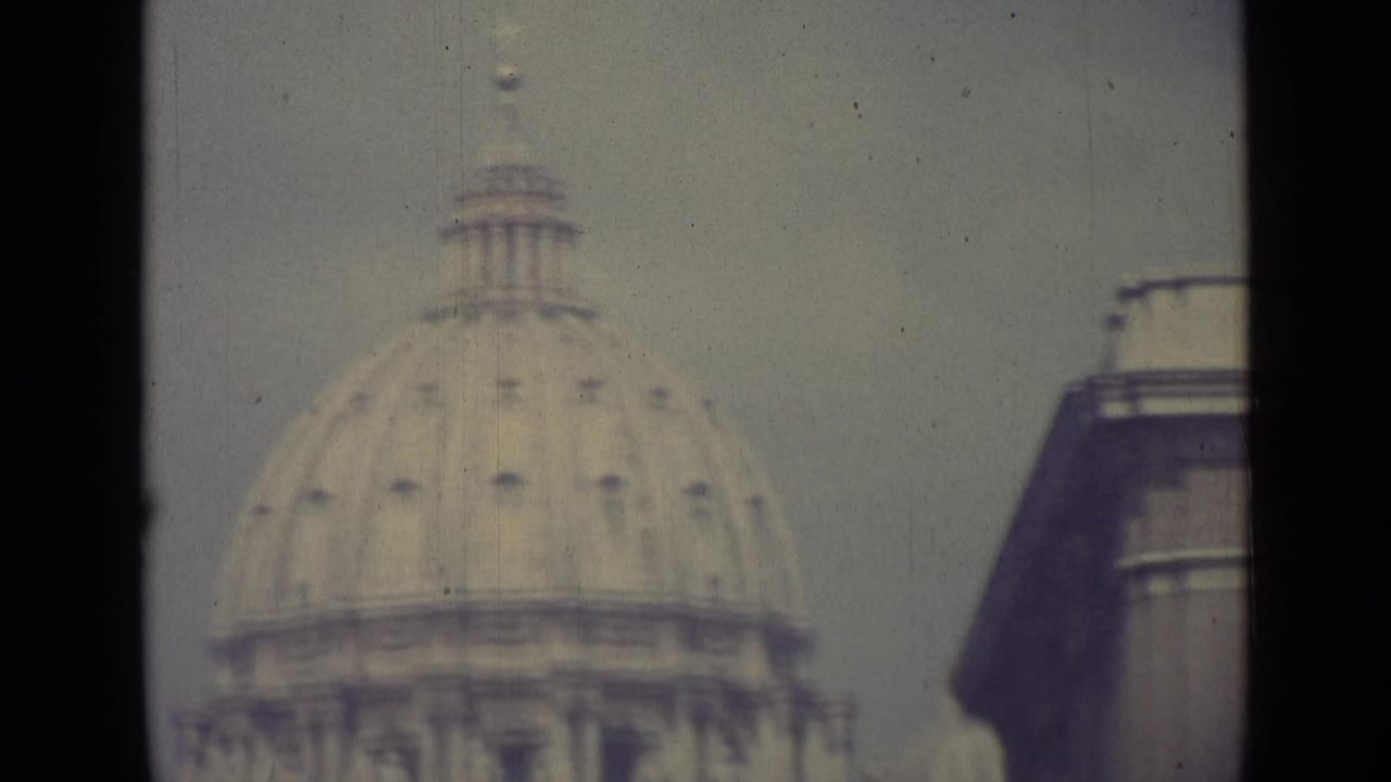1962 Vatican City frame with St. Peter's Basilica dome centered and a nearby building edge at right, softened by 8mm film grain.