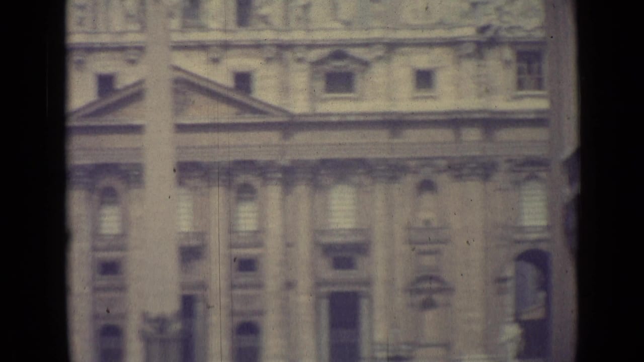 1962 Vatican City frame of the monumental facade, with stone columns, arched windows, and lower square activity partly visible.