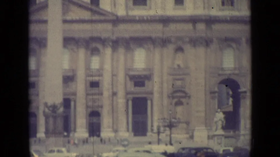 1962 Vatican City frame with the facade, statuary, cars, and small pedestrians visible through soft 8mm focus.