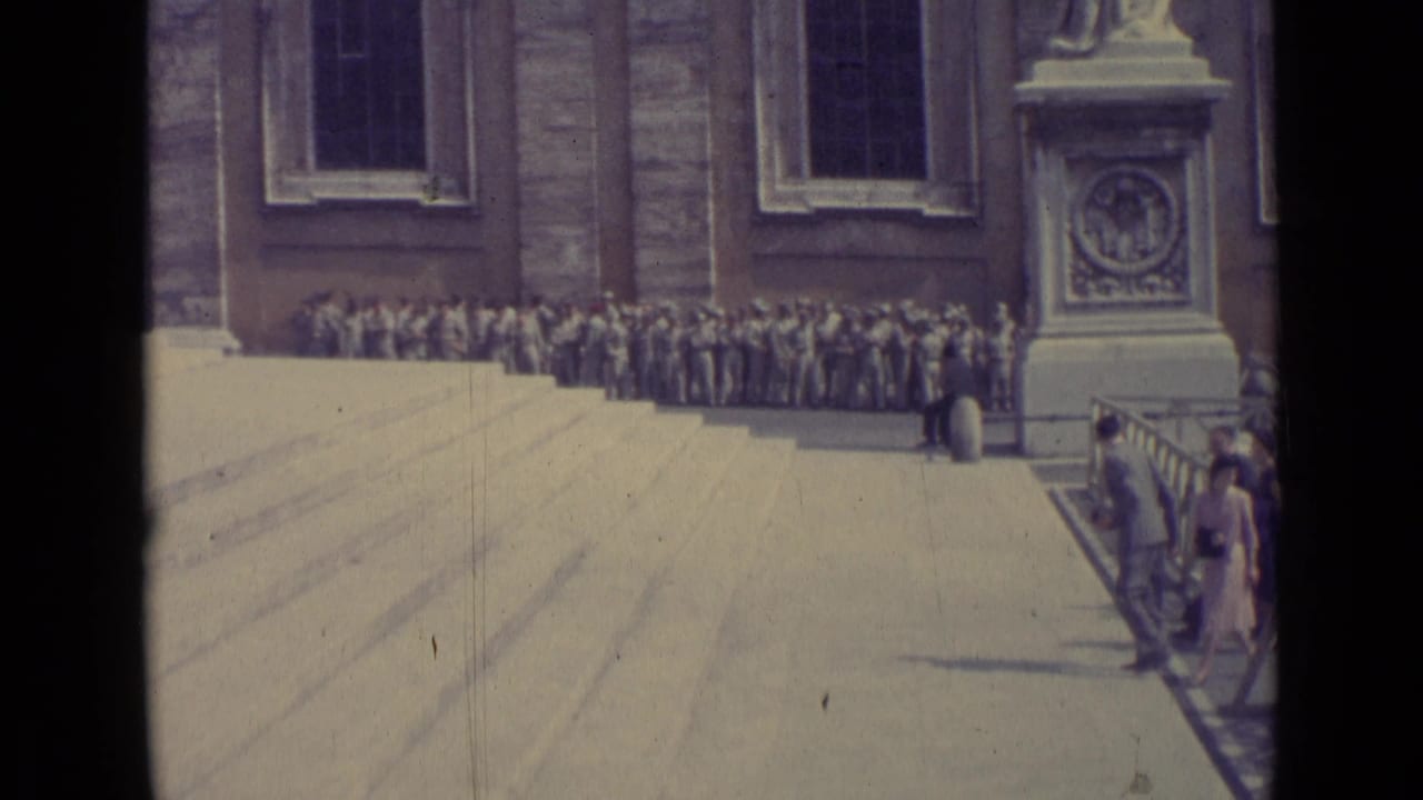 1962 Vatican City 8mm frame showing a gathered crowd along the building, with steps, pedestal detail, and visitors near the railing.