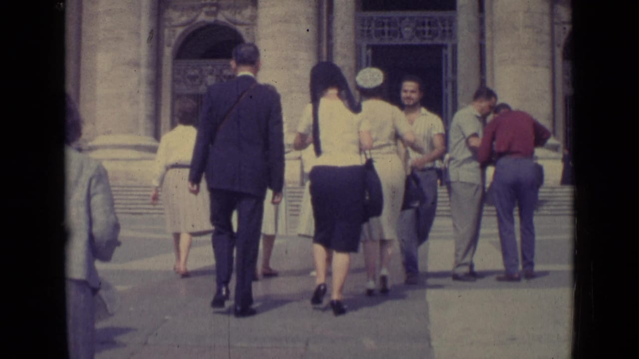 1962 Vatican City home-movie frame showing suited men and women in skirts walking toward an ornate stone entrance.