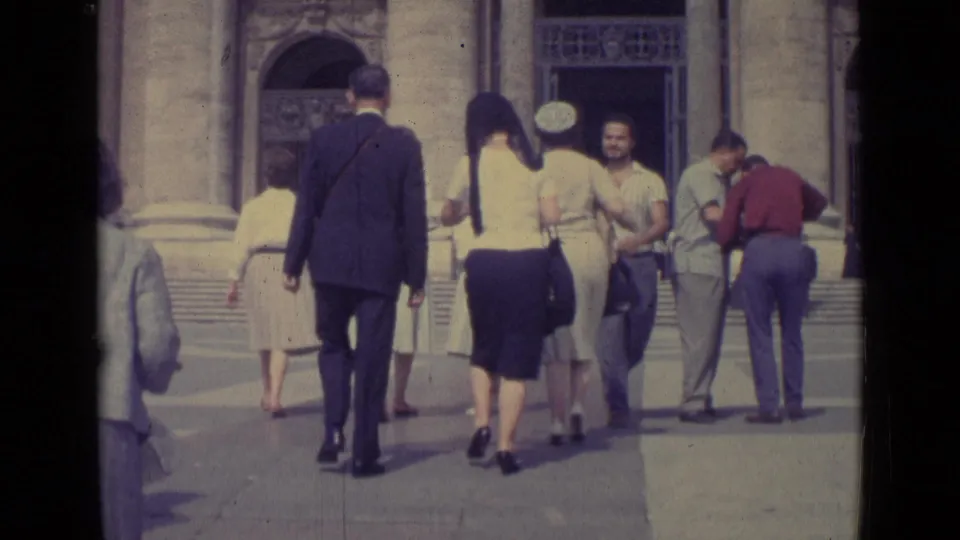 1962 Vatican City home-movie frame showing suited men and women in skirts walking toward an ornate stone entrance.