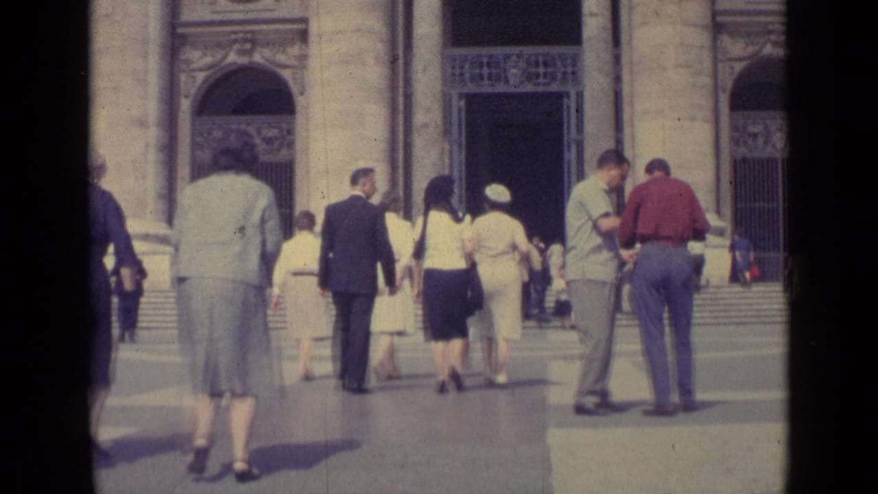 1962 Vatican City frame showing visitors from behind as they move toward broad steps and ornate arched doorways.