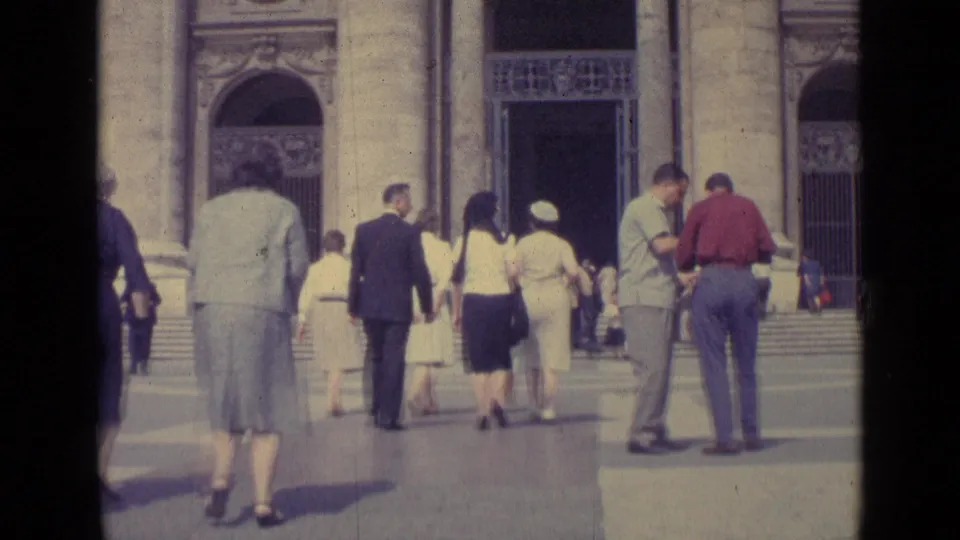 1962 Vatican City frame showing visitors from behind as they move toward broad steps and ornate arched doorways.