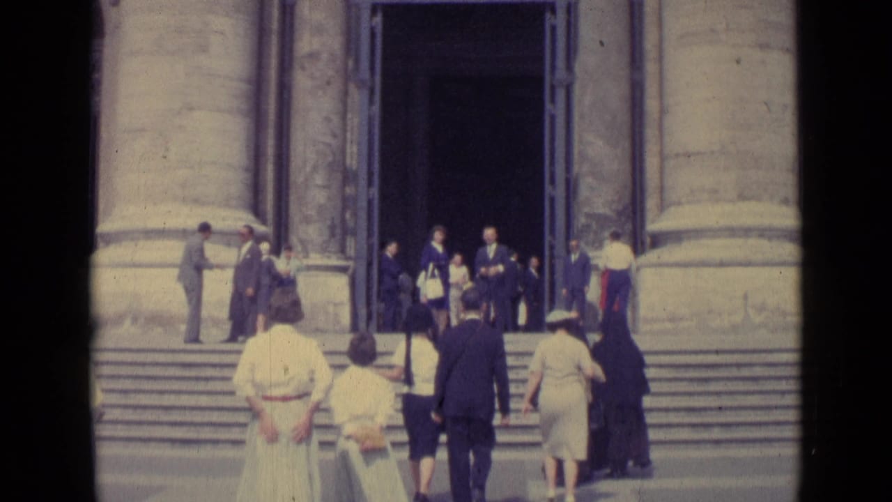 Visitors climb wide steps toward a large dark doorway between stone columns.