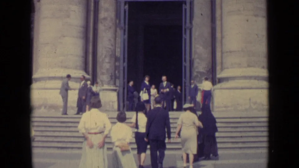 1962 Vatican City frame with tourists ascending basilica steps beneath massive stone columns and a dark entrance.