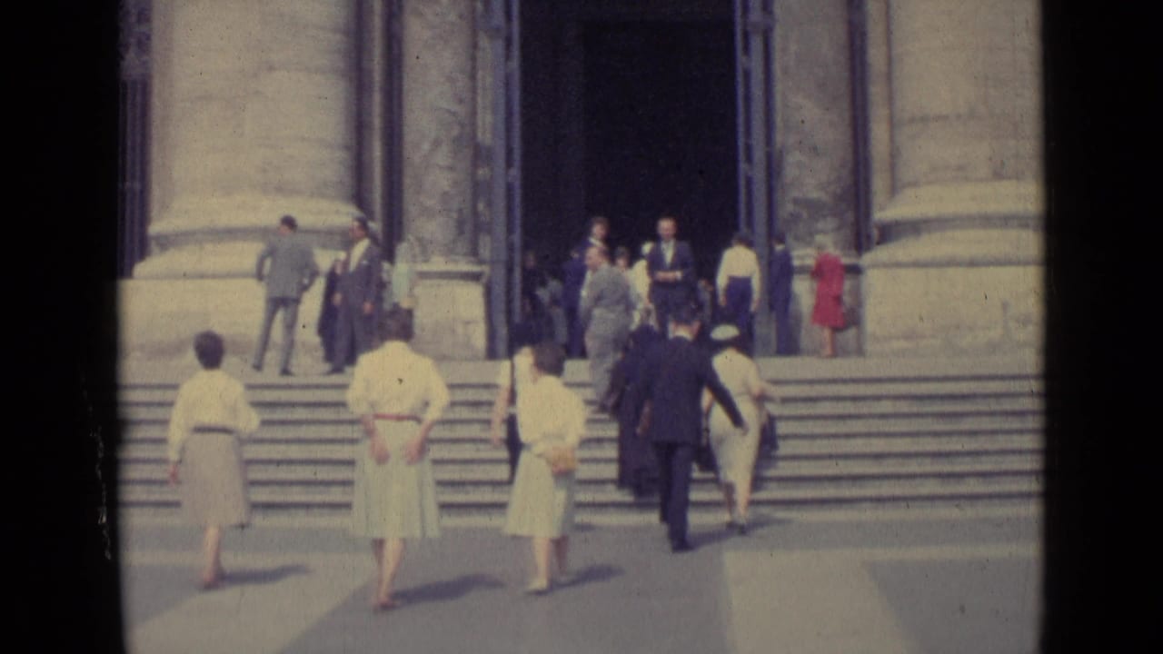 1962 Vatican City frame showing visitors in formal dress moving toward a basilica entrance with broad steps and columns.