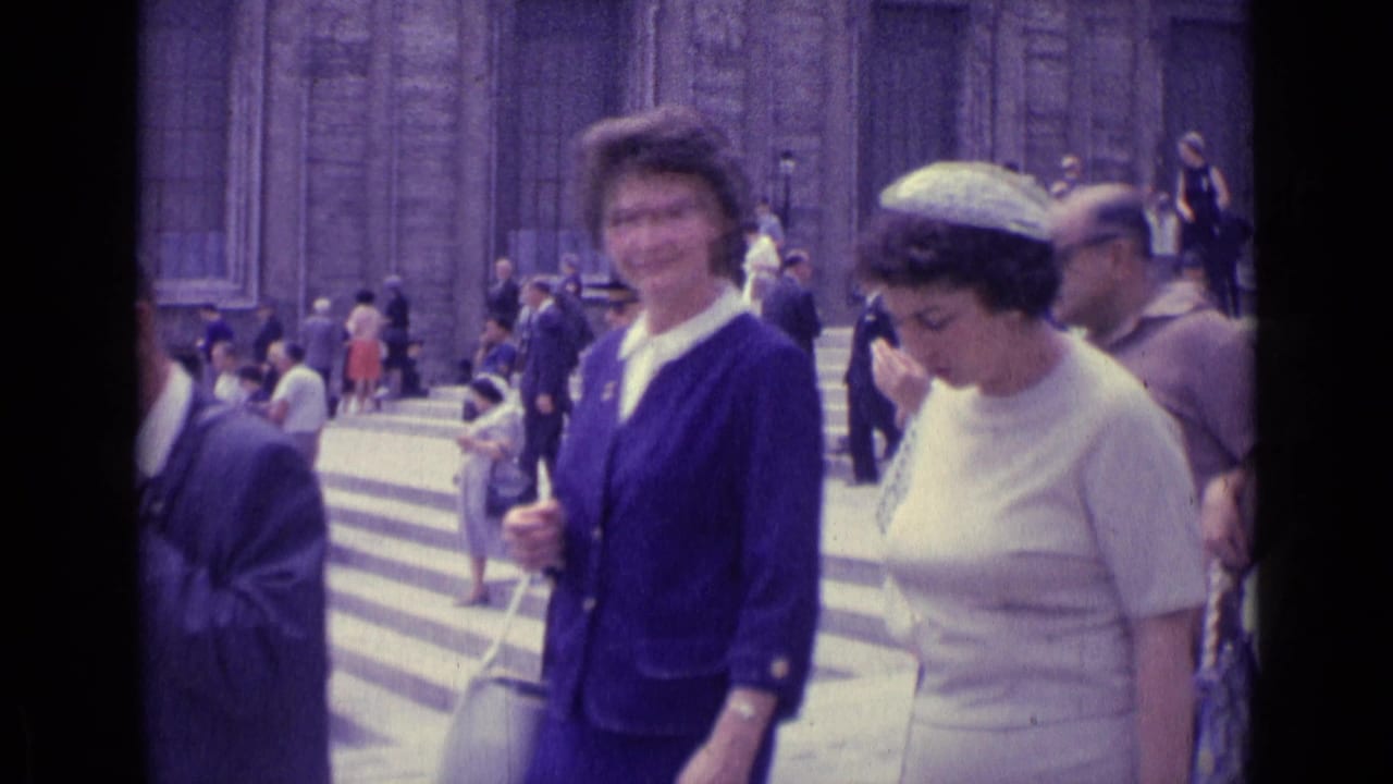 1962 Vatican City home-movie frame showing women in blue and white dresses walking close to the camera beside busy stone steps.